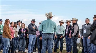 Man in a cowboy hat speaking to a group of people at a sale.