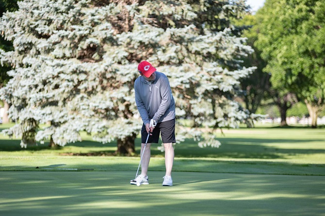 Man swinging at a golf ball on green golf course.