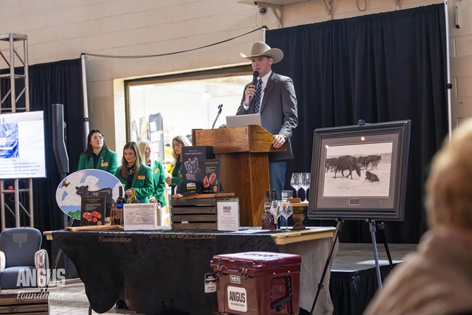 A man in a cowboy hat stands at the podium introducing the items available for auction at the Angus Foundation Herdsman Social.