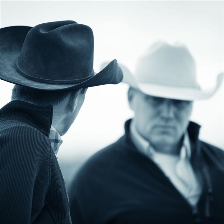 Two cattlemen in cowboy hats having a discussion.