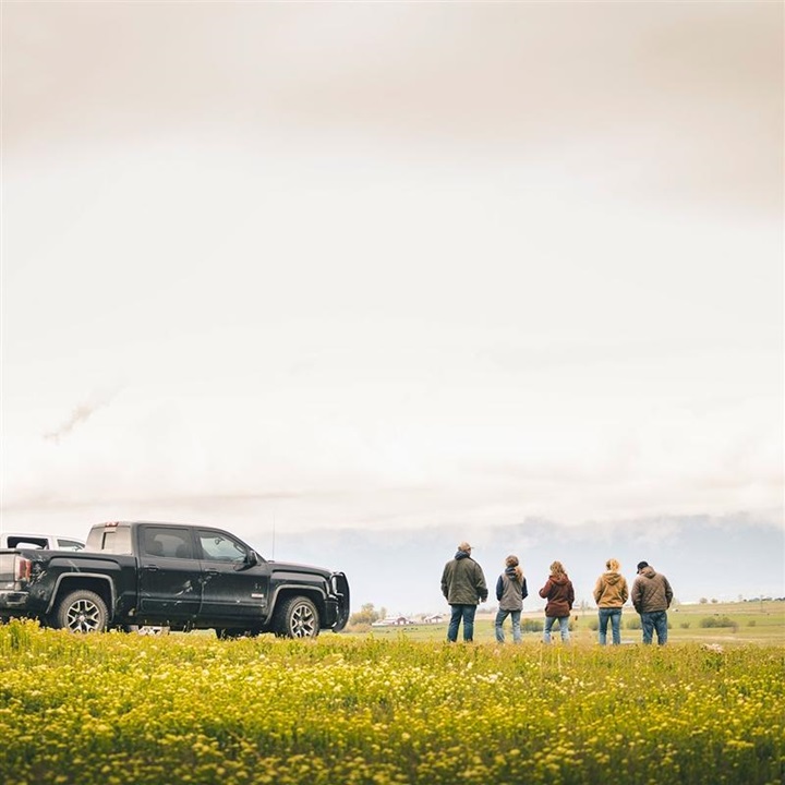 Family standing in a pasture with trucks.