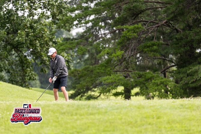 A golfer sizes up a shot from the rough while navigating the tree-lined course.