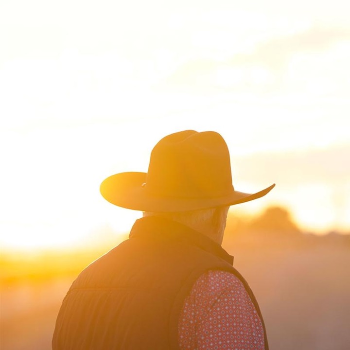 Cowboy in a hat looking away at the sunset.