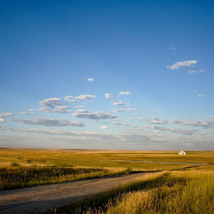 A vast midwestern landscape with a white barn off in the distance.