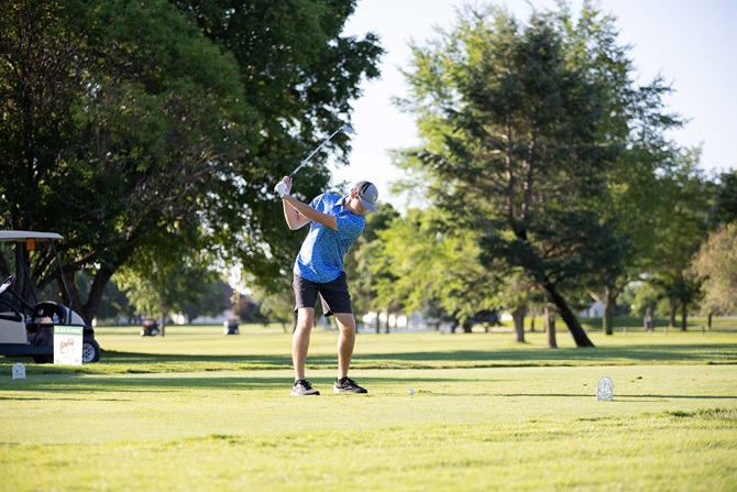 Man swinging at a golf ball on green golf course.