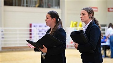 Two junior females in blazers presenting information at a contest at the National Junior Angus Show.