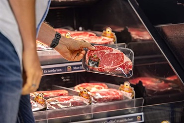 An individual picking up a Certified Angus Beef prime ribeye in the grocery store.