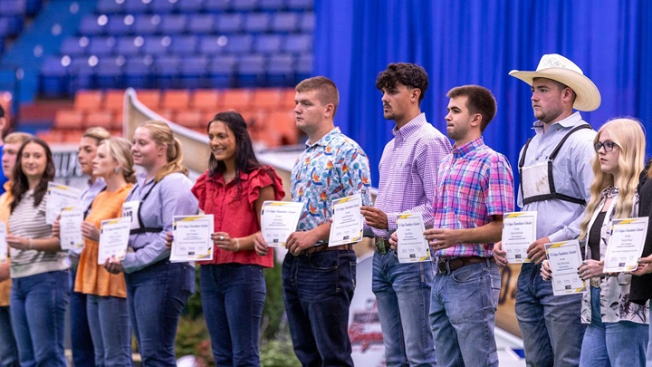 Scholarship recipients line the stage holding Angus Foundation scholarship certificates during an awards presentation.