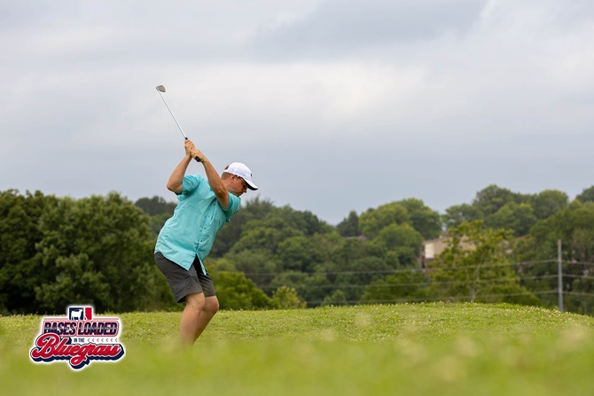 A participant follows through on a tee shot during the Bases Loaded in the Bluegrass golf tournament.