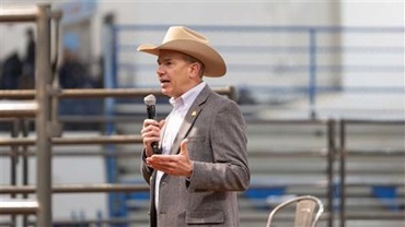 Man in a cowboy hat speaking on a microphone.