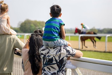 A family stands and watches a horse race.