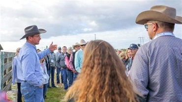 Man in a cowboy hat standing and presenting in front of a crowd of people outside