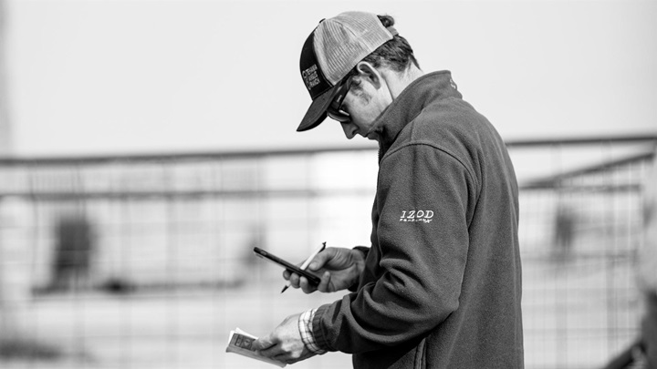 A cattle producer looking at a sale catalog and notes on his phone.