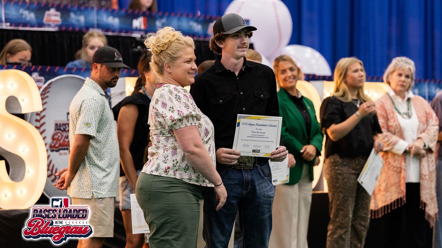 Scholarship recipient stands on stage holding an Angus Foundation scholarship certificate during the scholarship presentations at the National Junior Angus Show.
