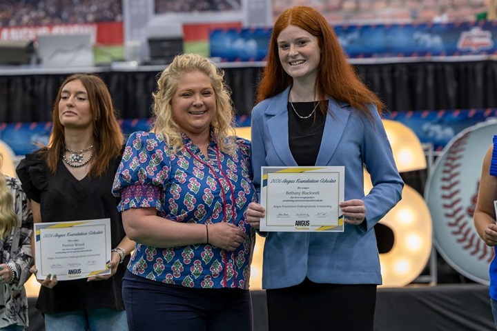 An Angus Foundation undergraduate scholarship recipient poses with a presenter while holding a scholarship certificate.