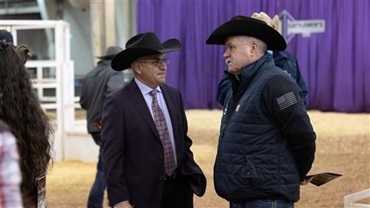 Two men in cowboy hats speaking to one another.