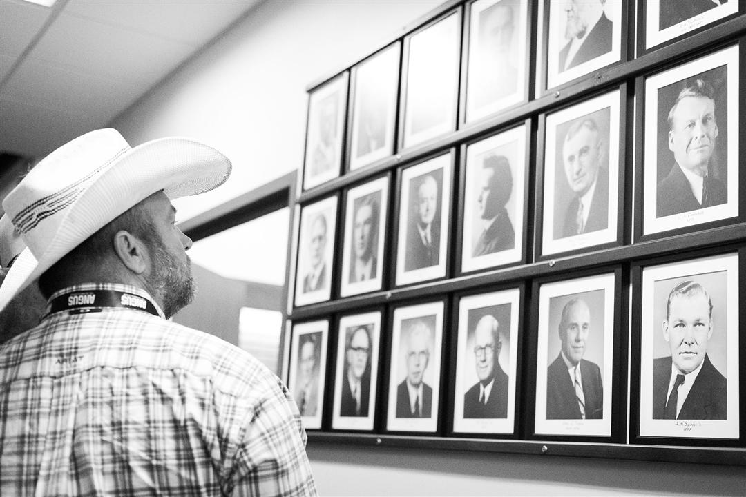 A man in a cowboy hat looking at a historic wall of individuals at the American Angus Association office.
