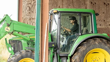A student intern drives a tractor to put out hay for cattle on the farm he is working at for the summer.