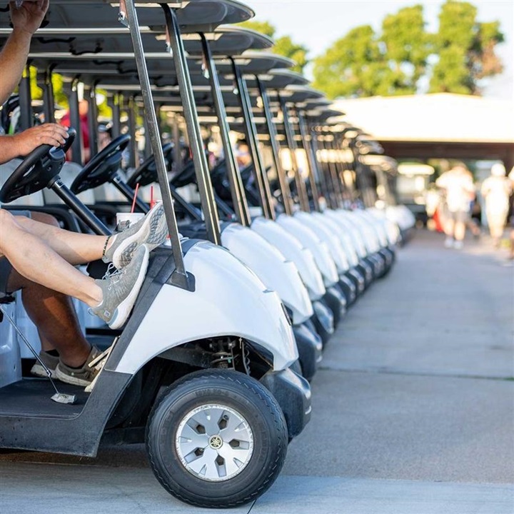 Golf carts lined up in a row at a golf course awaiting start time.