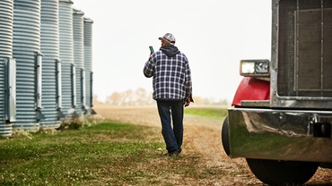 Man walking outside along the large grain storage silos on farm - stock photo