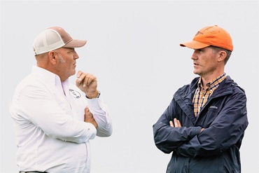 Two men in ball caps speaking to one another.