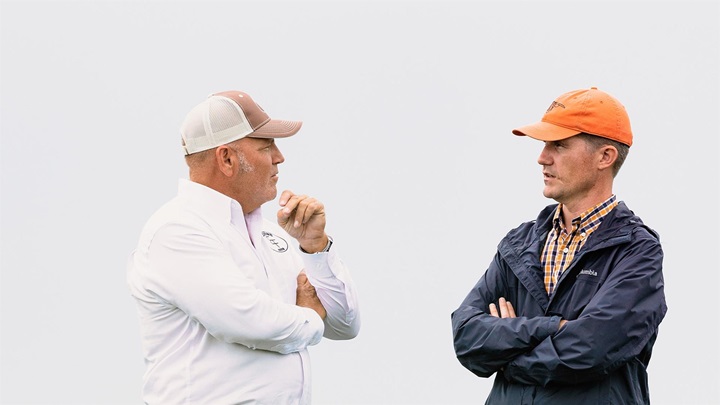 Two men in ball caps speaking to one another.