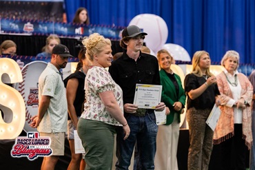 Scholarship recipient stands on stage holding an Angus Foundation scholarship certificate during the scholarship presentations at the National Junior Angus Show.