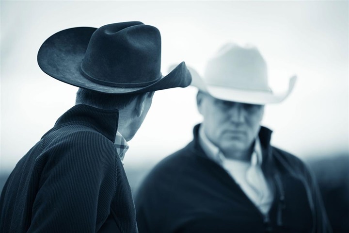 Two cattlemen in cowboy hats having a discussion.