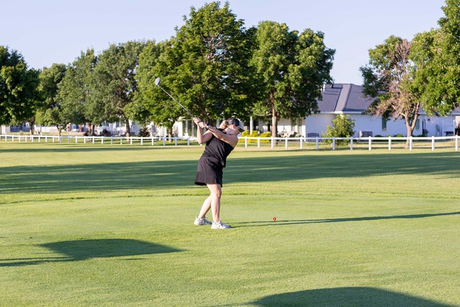 Woman taking a swing at a ball on the golf course.