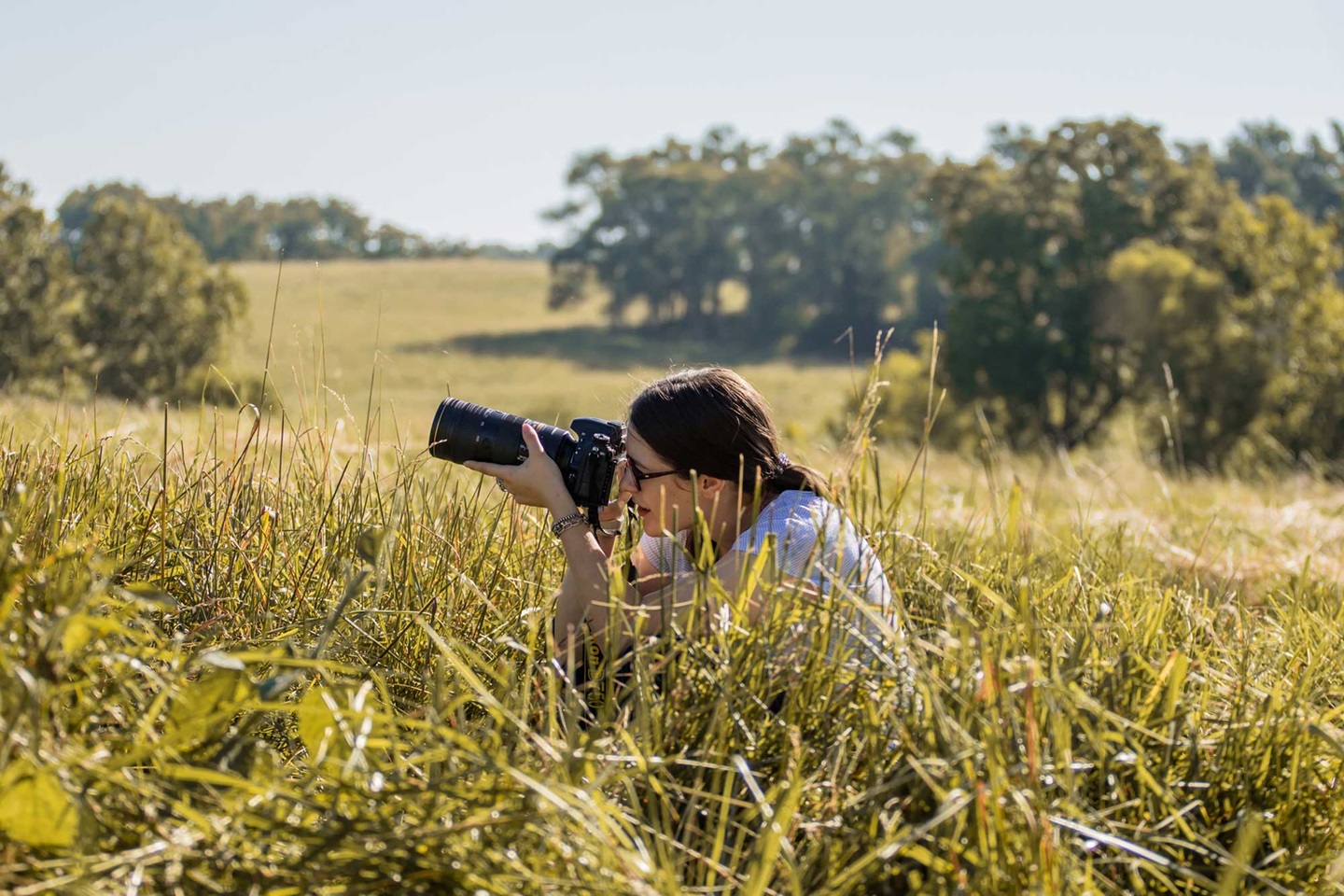 A woman crouches in a field with a camera in her hands 