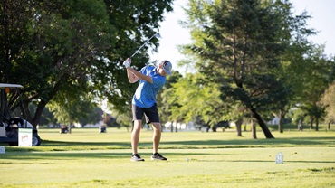 Man on a golf course swinging a golf club.