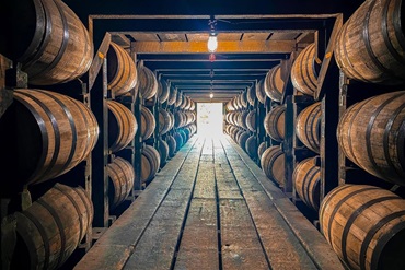 A room full of whiskey barrels in Kentucky with a light shining at the end of the long barn.