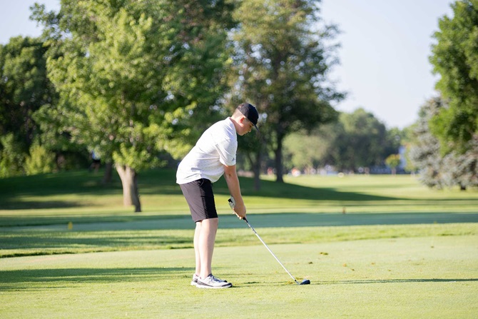 Man swinging at a golf ball on green golf course.