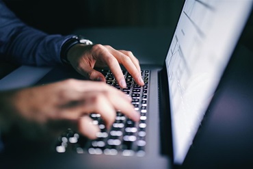 An individual typing on a laptop computer looking through a database.