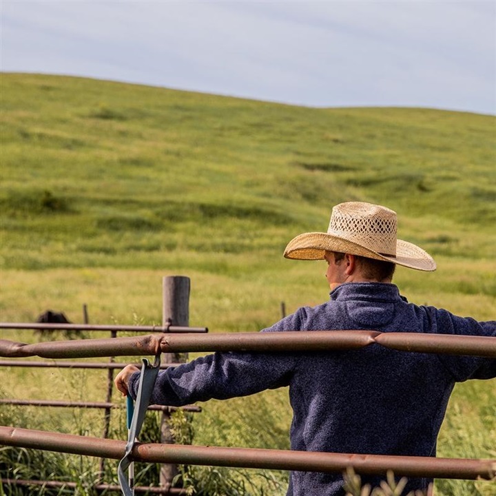 Young man in a cowboy had leaning on a fence in a pasture.