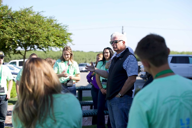 A man in sunglasses and a vest speaking to a group of NJAA members outside during a tour stop at the 2023 LEAD Conference.