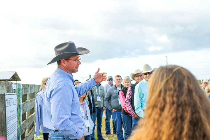 A man in a cowboy hat speaks to a large group of people outside.