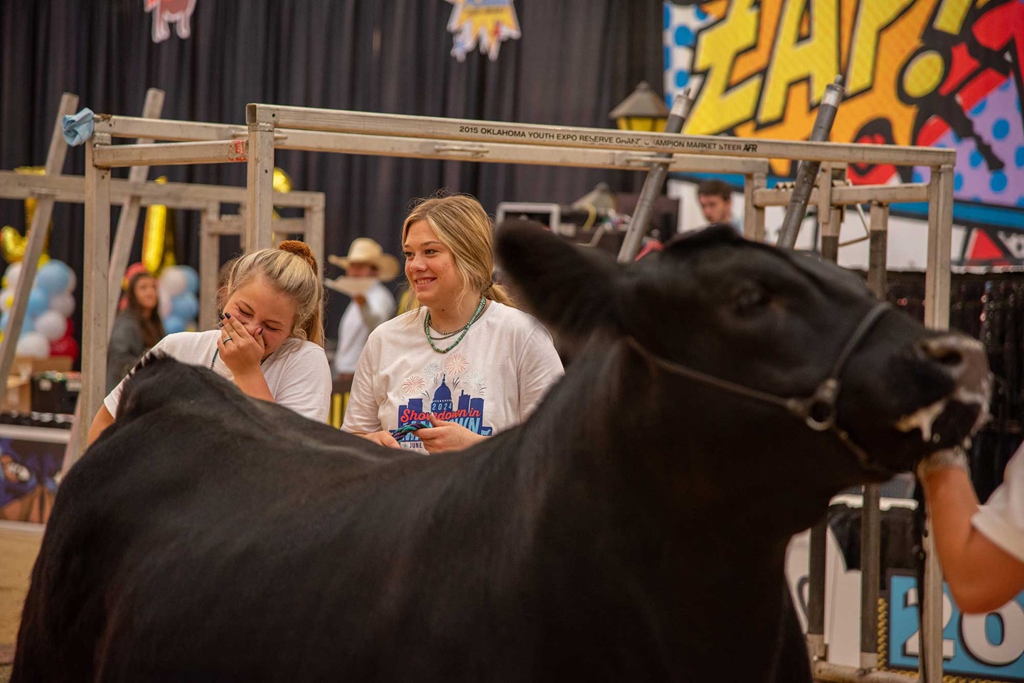 Two girls smile while standing behind and Angus cow