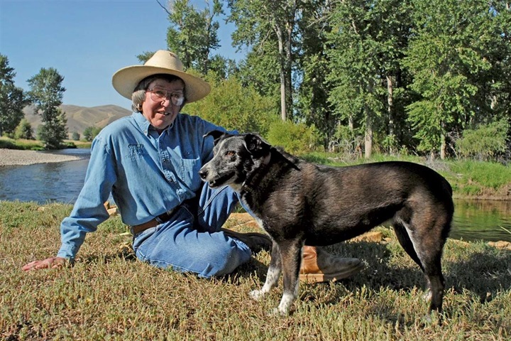 Cam Cooper sitting next to a lake with her dog.