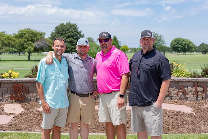 Group of four men on a golf course standing together smiling.