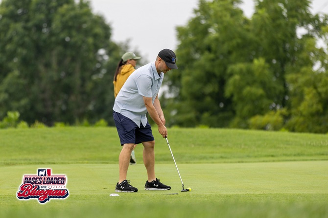 A golfer focuses on a putt while another participant watches from behind the green.