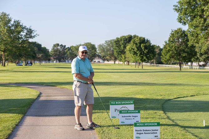 Individual standing in front of sponsor signs on green golf course.