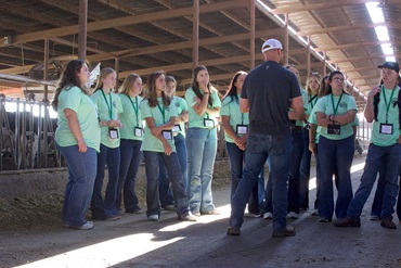 Group of NJAA members listening to a presenter in a free-stall barn at a dairy.