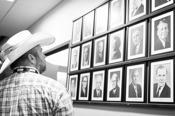 A man in a cowboy hat looking at a historic wall of individuals at the American Angus Association office.