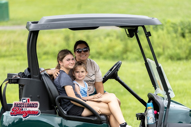 Spectators enjoy the day from a golf cart while following action around the course.