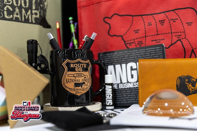 Close-up of Angus-branded promotional merchandise including a commemorative mug, pens, and accessories.