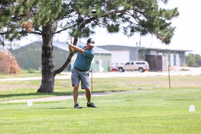 Man swinging golf club at a golf course.