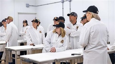 Group of adults in smocks standing in a meat lab.