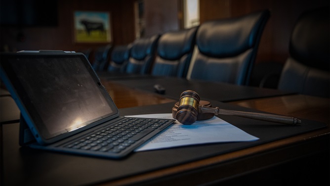 Image of a tablet and gavel sitting on a table in a board room.