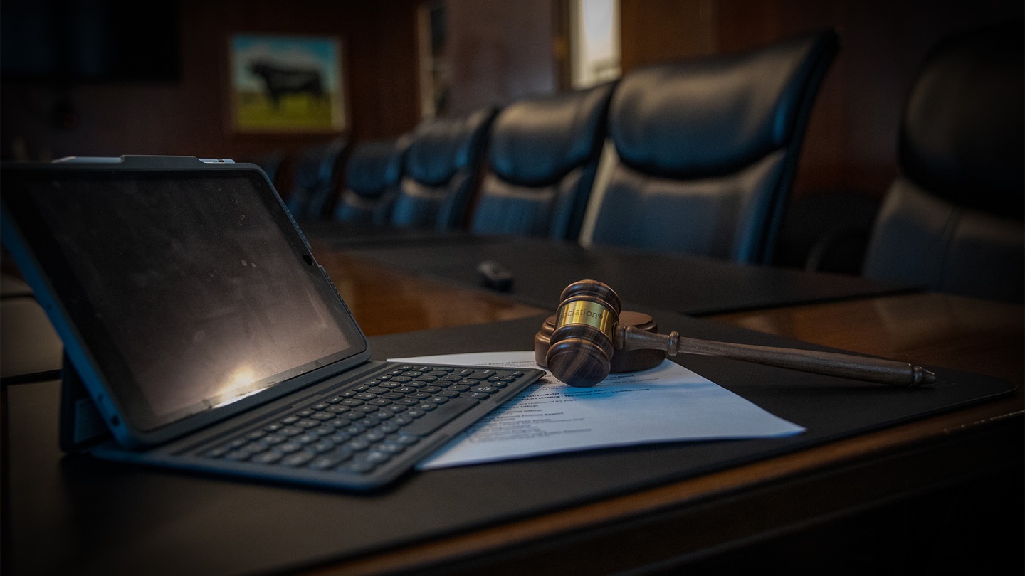 Image of a tablet and gavel sitting on a table in a board room.
